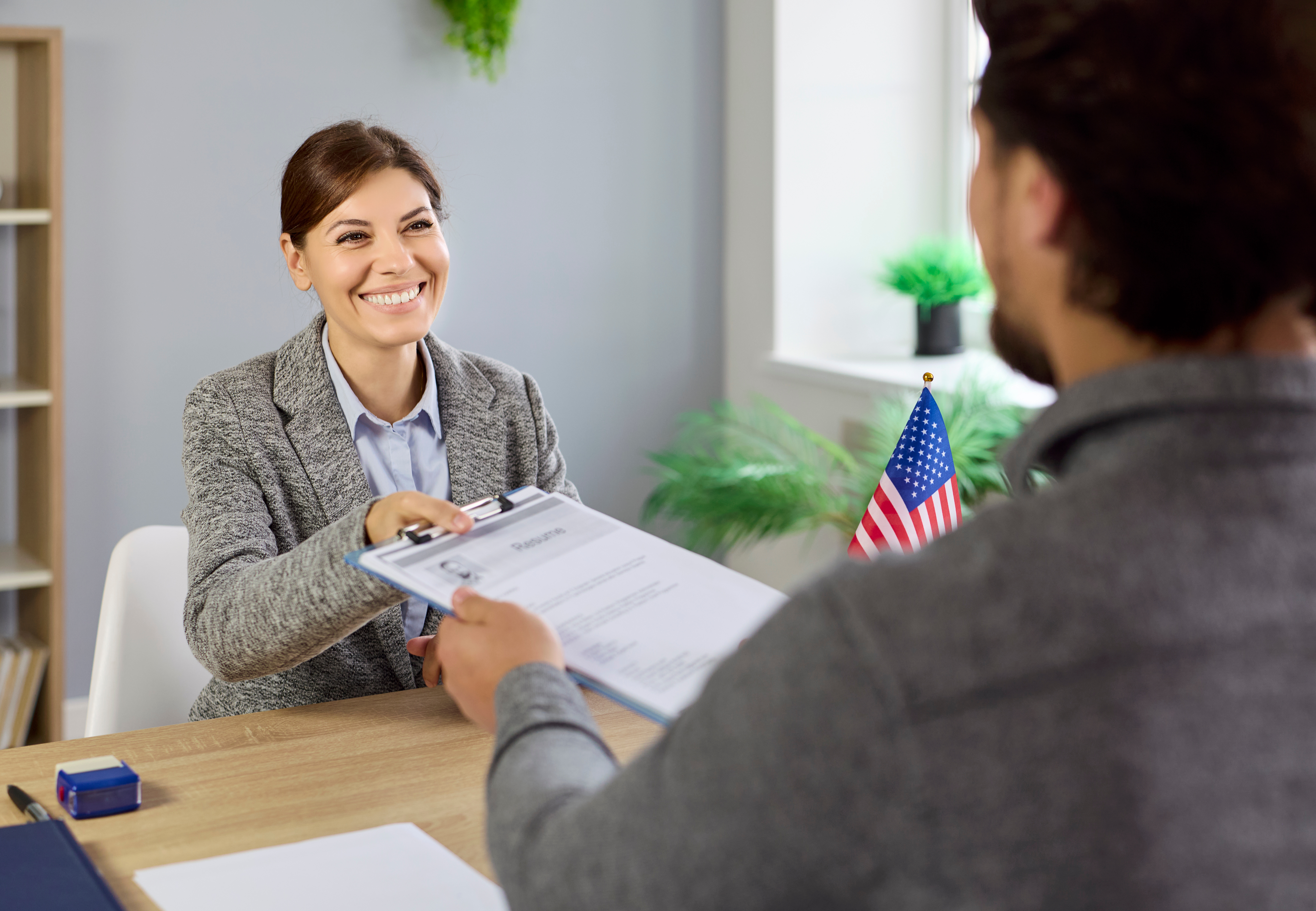 Professional representative handing documents to a candidate with a U.S. flag visible in the background, representing successful consular preparation and candidate support